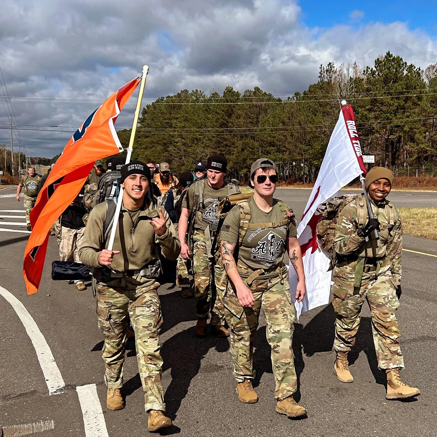 People dressed in military uniforms walking down a road with a University of Alabama and Auburn University flag.